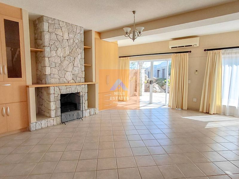 Spacious living room featuring a stone fireplace, built-in cabinetry, tiled flooring, and direct access to the outdoor area through sliding glass doors.