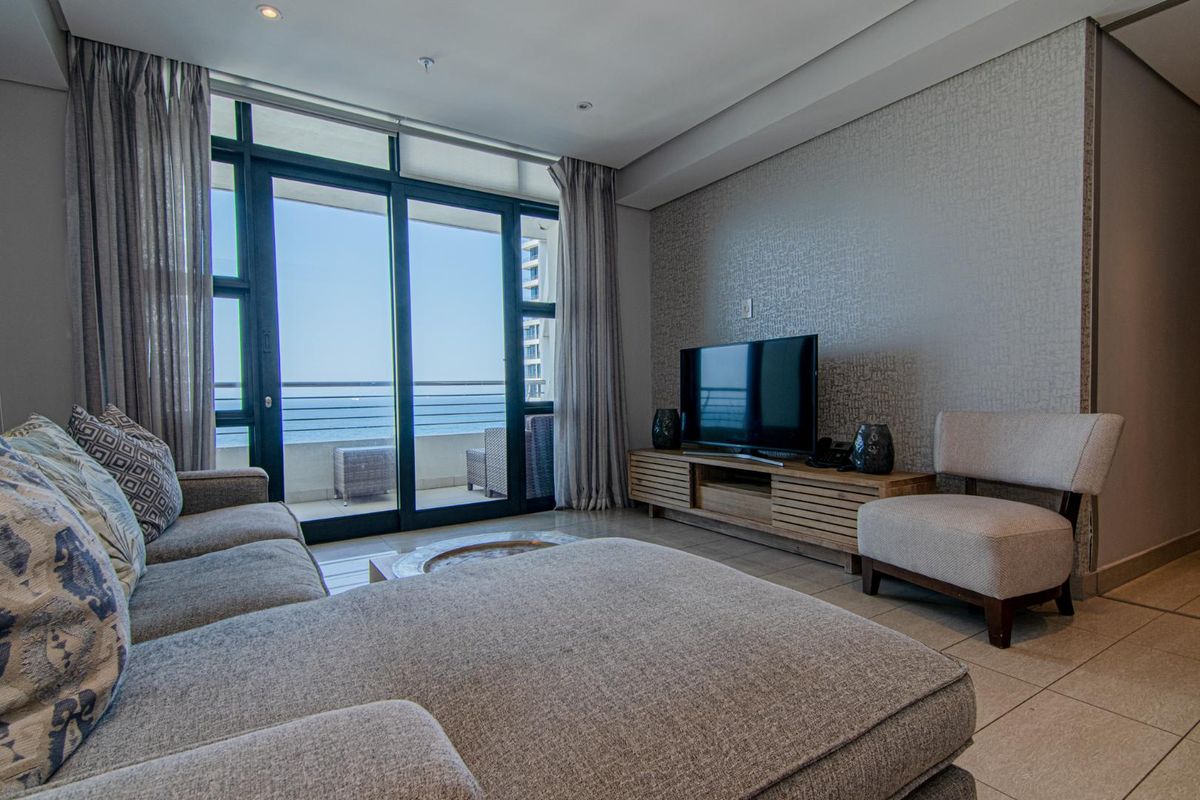 A modern living room featuring large sliding glass doors that open onto a balcony with ocean views, complemented by tiled flooring and textured wallpaper.