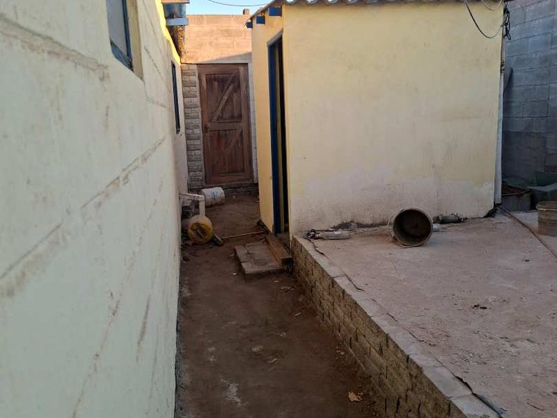 A narrow rear exterior area featuring concrete paving, a cinder block boundary wall, and a small outbuilding with corrugated roof sheeting.