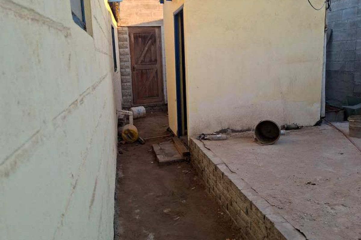 A narrow rear exterior area featuring concrete paving, a cinder block boundary wall, and a small outbuilding with corrugated roof sheeting.