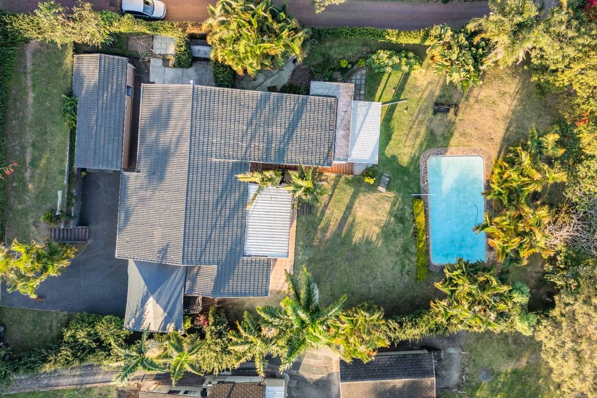 Aerial view of the property featuring a swimming pool, landscaped garden, tiled roof, and driveway access.
