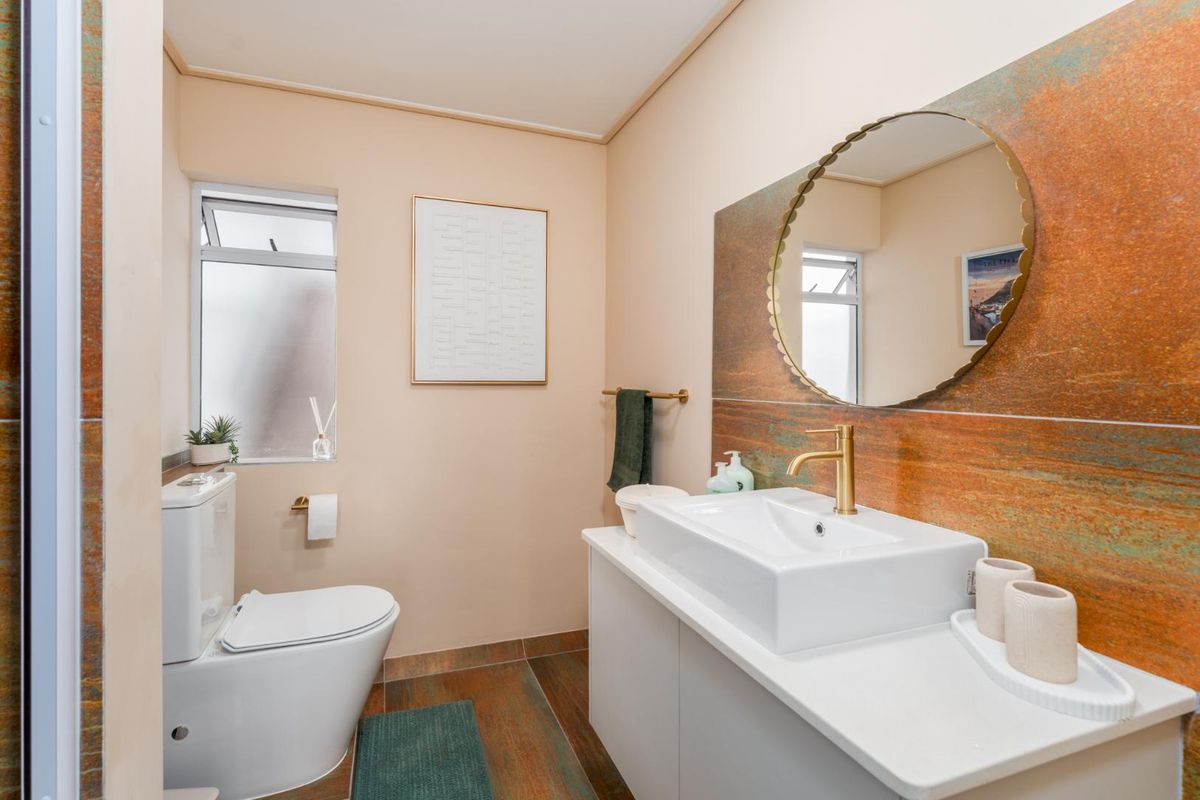 Modern bathroom featuring a vessel sink vanity, gold-toned faucet, wall-mounted mirror, and distinctive rust-effect wall tiling.