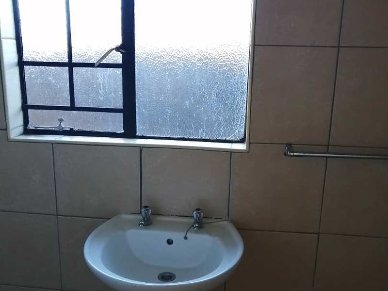 A functional bathroom featuring a pedestal basin, tiled walls, and a window with security bars.
