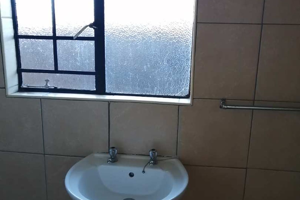 A functional bathroom featuring a pedestal basin, tiled walls, and a window with security bars.