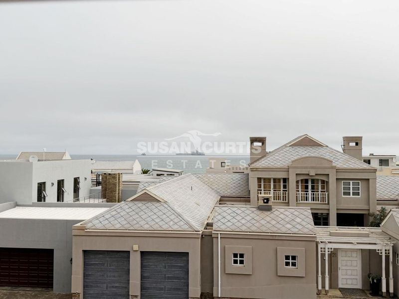 Aerial view of a residential property featuring a tiled roof, double garage, and balcony with a distant ocean view.