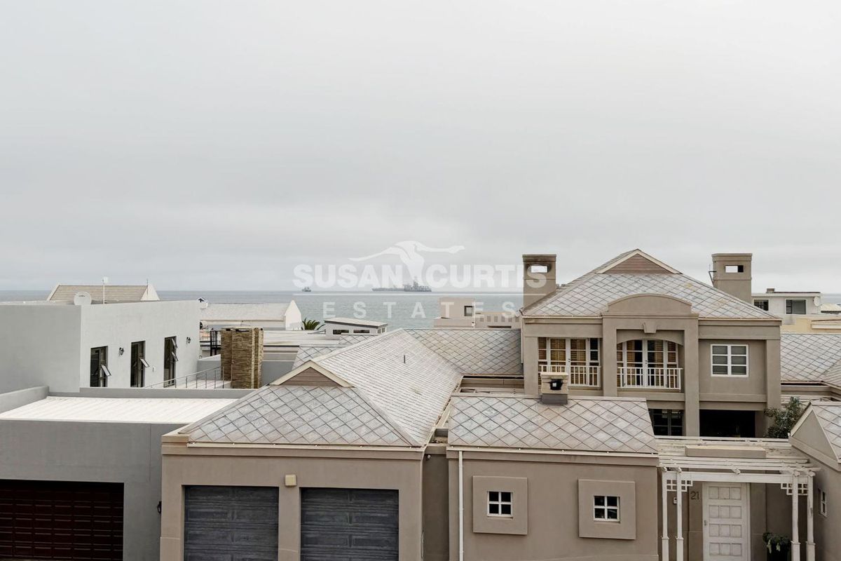 Aerial view of a residential property featuring a tiled roof, double garage, and balcony with a distant ocean view.