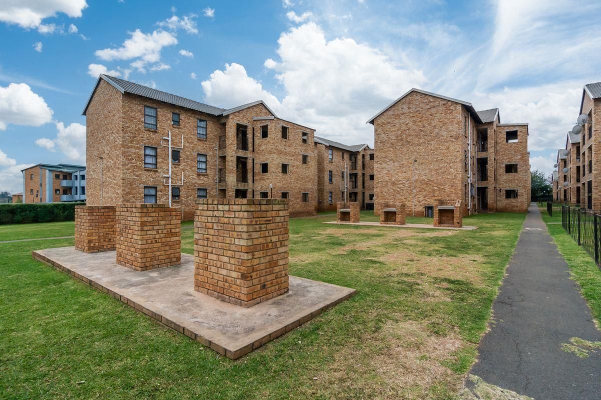 Exterior view of a residential apartment complex featuring face brick buildings, communal garden areas, and built-in brick braai facilities.