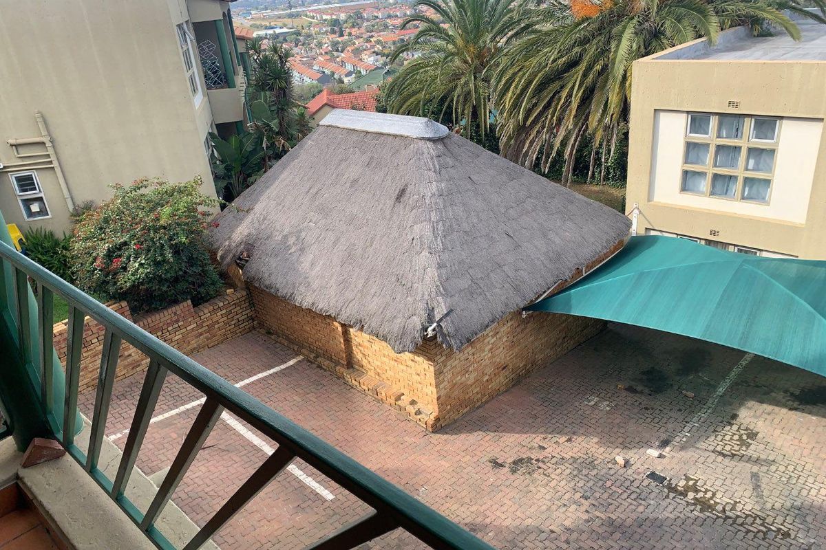 Elevated view of a communal courtyard area featuring a structure with a thatched roof, brick paving, and a green shade sail.