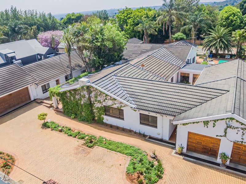 Aerial view of a residential property featuring a large paved driveway, multiple garages, and a well-maintained tiled roof structure.