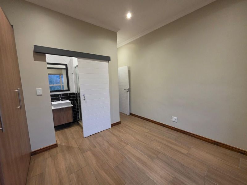 A spacious, empty bedroom featuring modern wood-look tiled flooring, built-in cupboards, and a sliding barn door providing access to an en-suite bathroom.