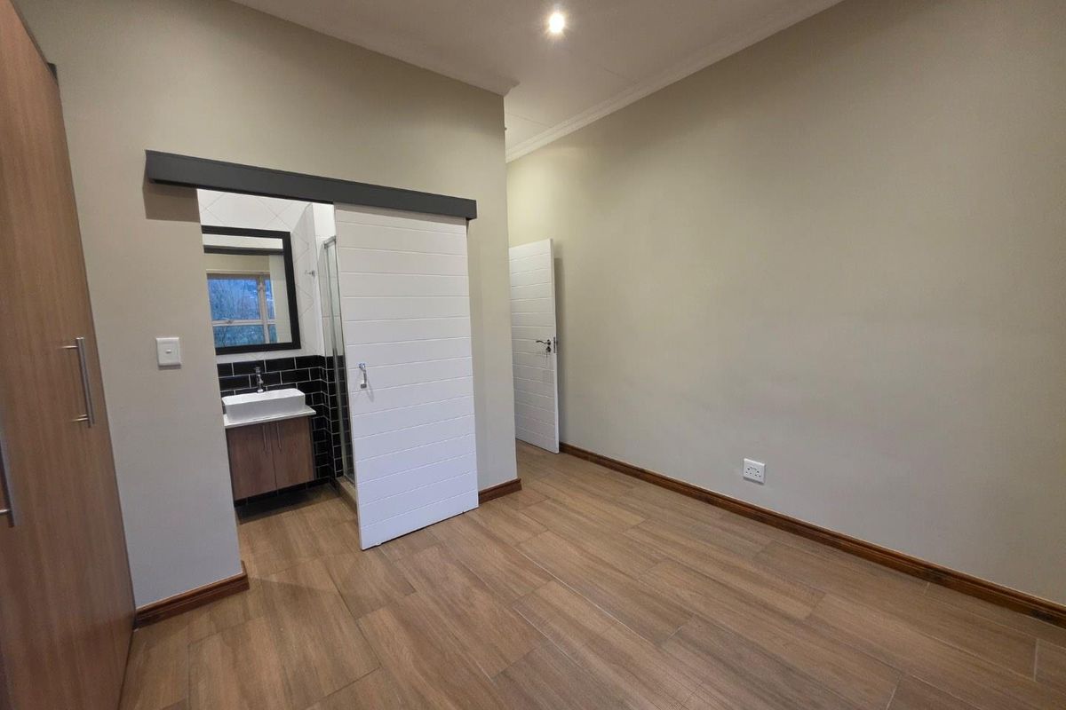A spacious, empty bedroom featuring modern wood-look tiled flooring, built-in cupboards, and a sliding barn door providing access to an en-suite bathroom.