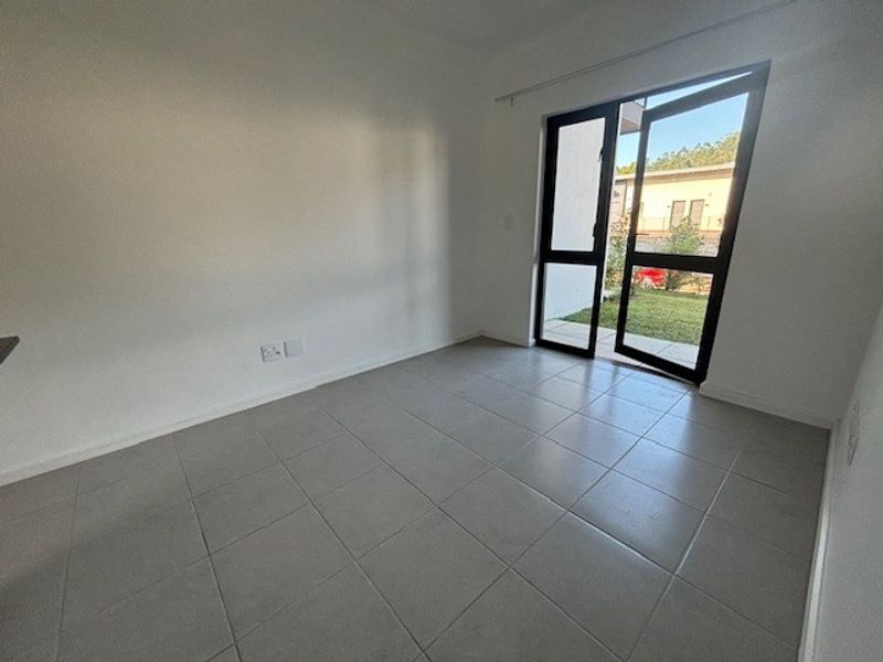 A bright, empty bedroom featuring neutral tiled flooring and a large glass door providing direct access to the outdoor area.