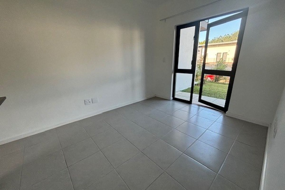 A bright, empty bedroom featuring neutral tiled flooring and a large glass door providing direct access to the outdoor area.