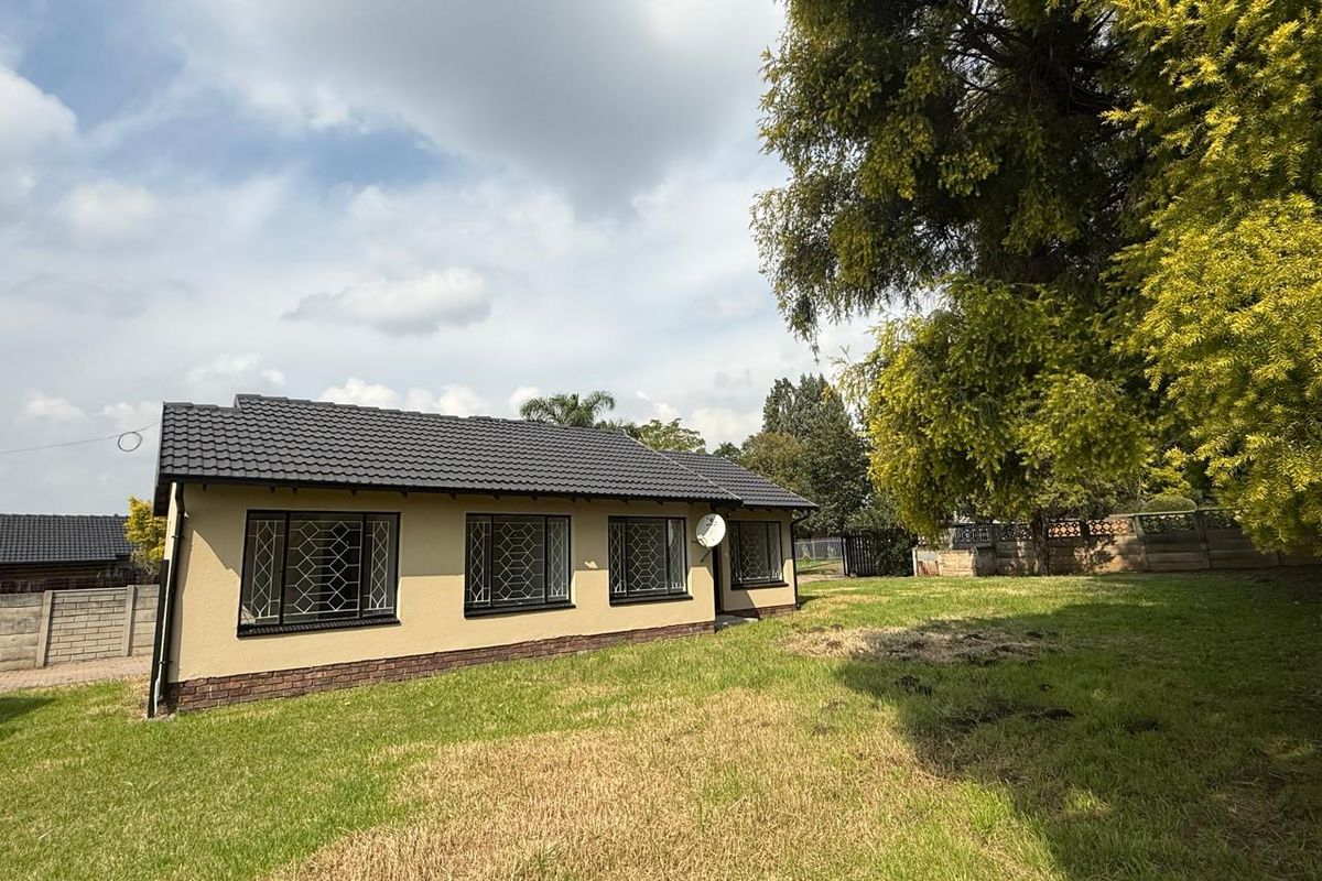 A view of the exterior rear of the house, featuring a tiled roof, security-grilled windows, and a spacious surrounding lawn area.
