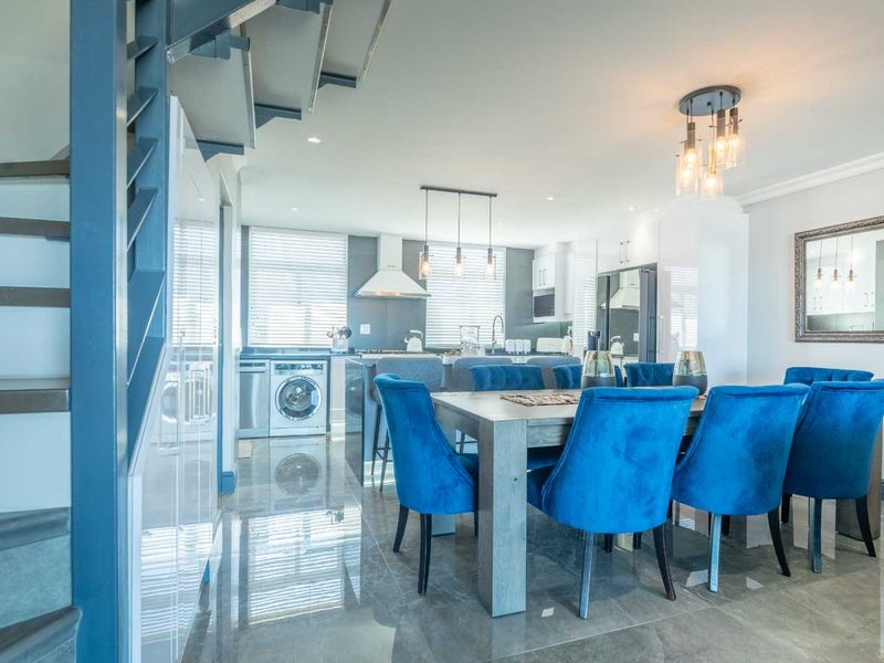 Modern open-plan kitchen and dining area featuring sleek cabinetry, integrated appliances, polished tile flooring, and a contemporary staircase.