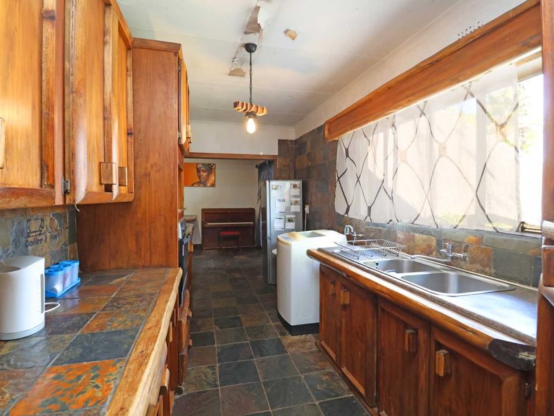 A dated kitchen featuring wooden cabinetry, slate tile countertops, and flooring, with visible ceiling damage requiring repair and modernization.