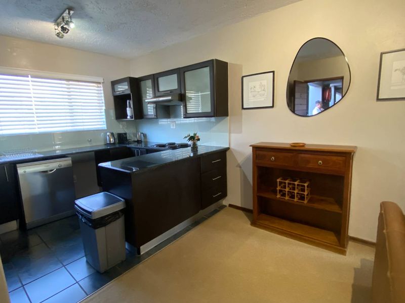 A functional kitchen featuring dark wood cabinetry, black granite countertops, integrated dishwasher, and a glass splashback, offering a clean and practical workspace.