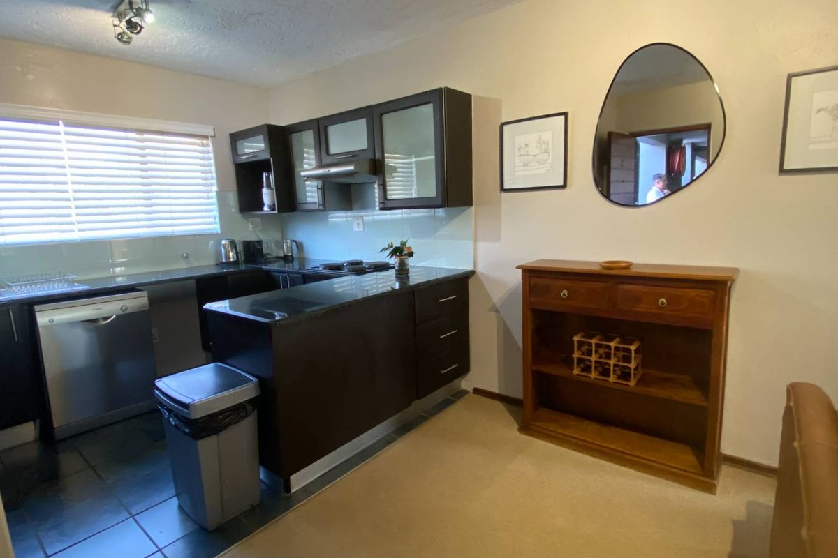 A functional kitchen featuring dark wood cabinetry, black granite countertops, integrated dishwasher, and a glass splashback, offering a clean and practical workspace.
