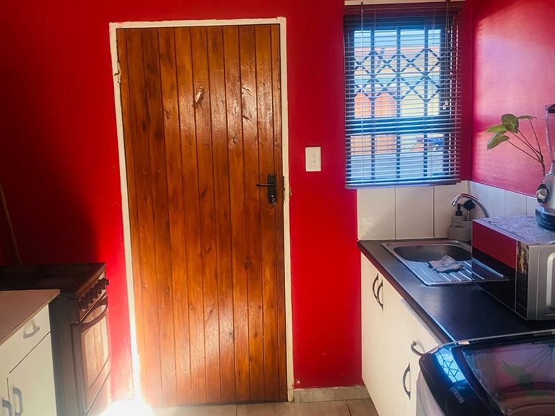 A functional kitchen featuring built-in cabinetry, a stainless steel sink, tiled flooring, and a secure wooden door with a security gate.
