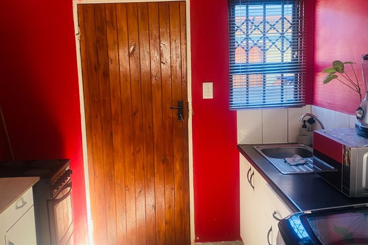 A functional kitchen featuring built-in cabinetry, a stainless steel sink, tiled flooring, and a secure wooden door with a security gate.