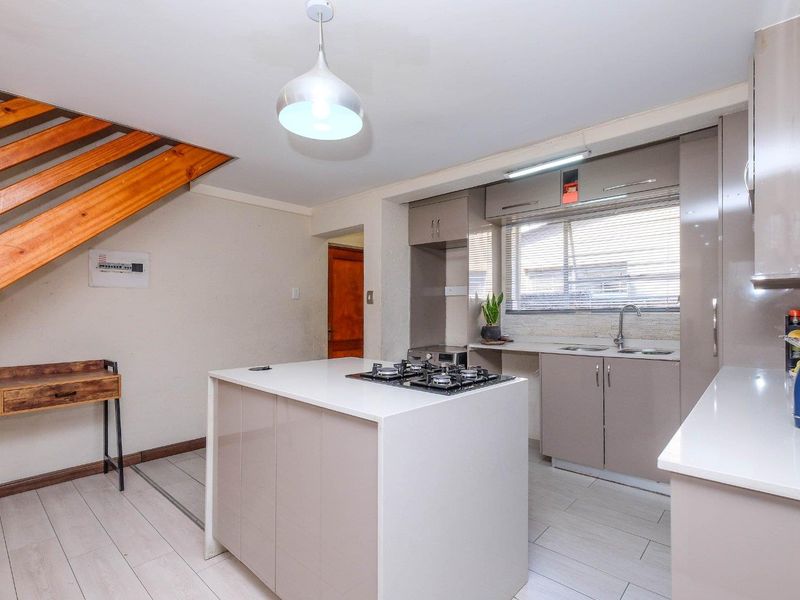 Modern kitchen featuring a central island with a gas hob, sleek cabinetry, stainless steel sink, and light laminate flooring, adjacent to an open staircase.
