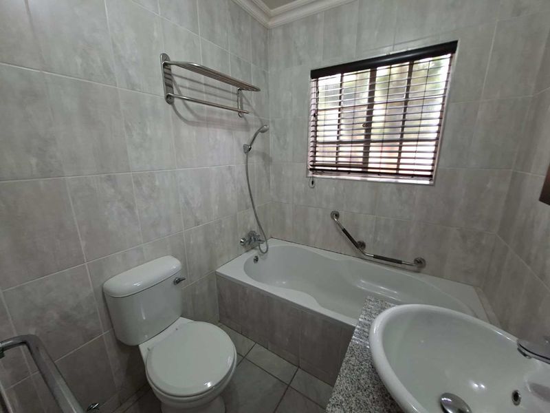 A clean, functional bathroom featuring a bathtub with shower attachment, vanity basin with granite countertop, and neutral wall tiling.