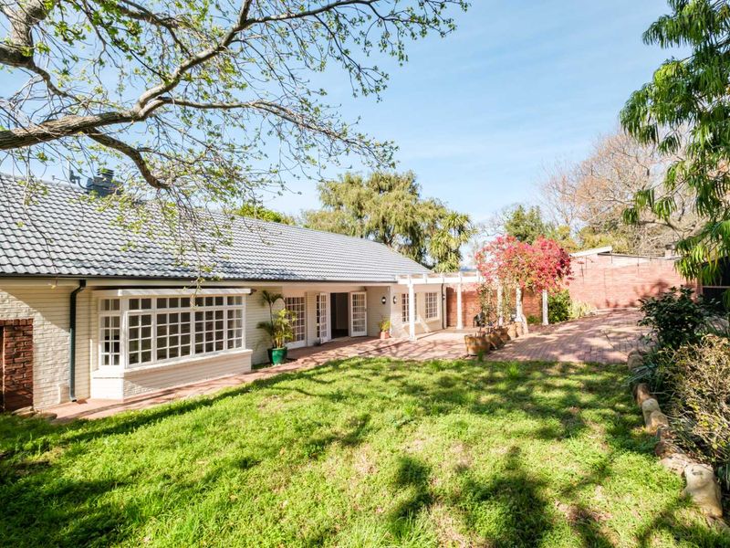 Rear view of the house featuring a spacious brick patio, pergola, and a well-maintained garden with mature trees.