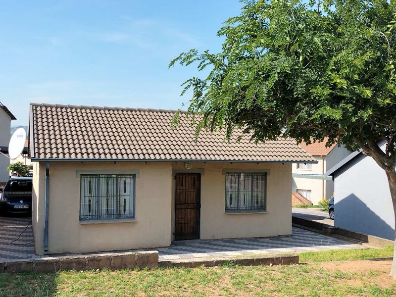 Front elevation of a single-story house featuring a tiled roof, security bars on windows, and a paved patio area.