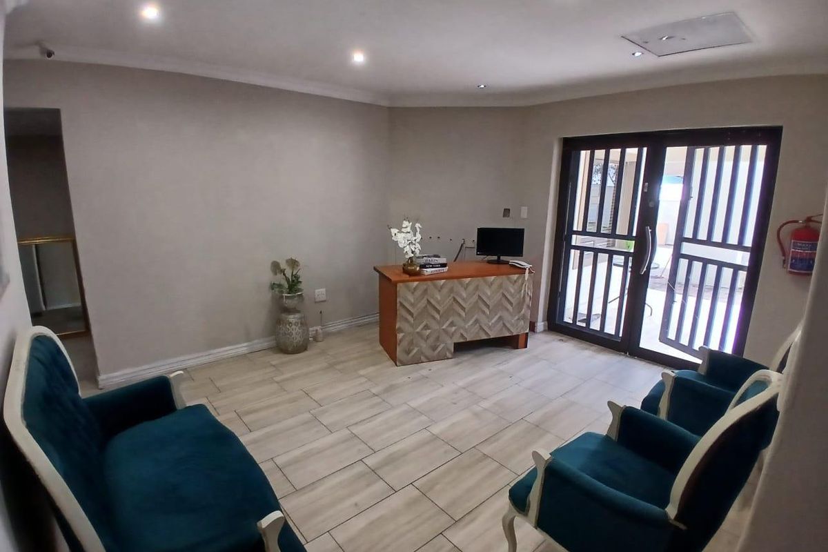 A well-lit office or reception area featuring tiled flooring, recessed ceiling lights, and a secure glass door with a metal security gate.