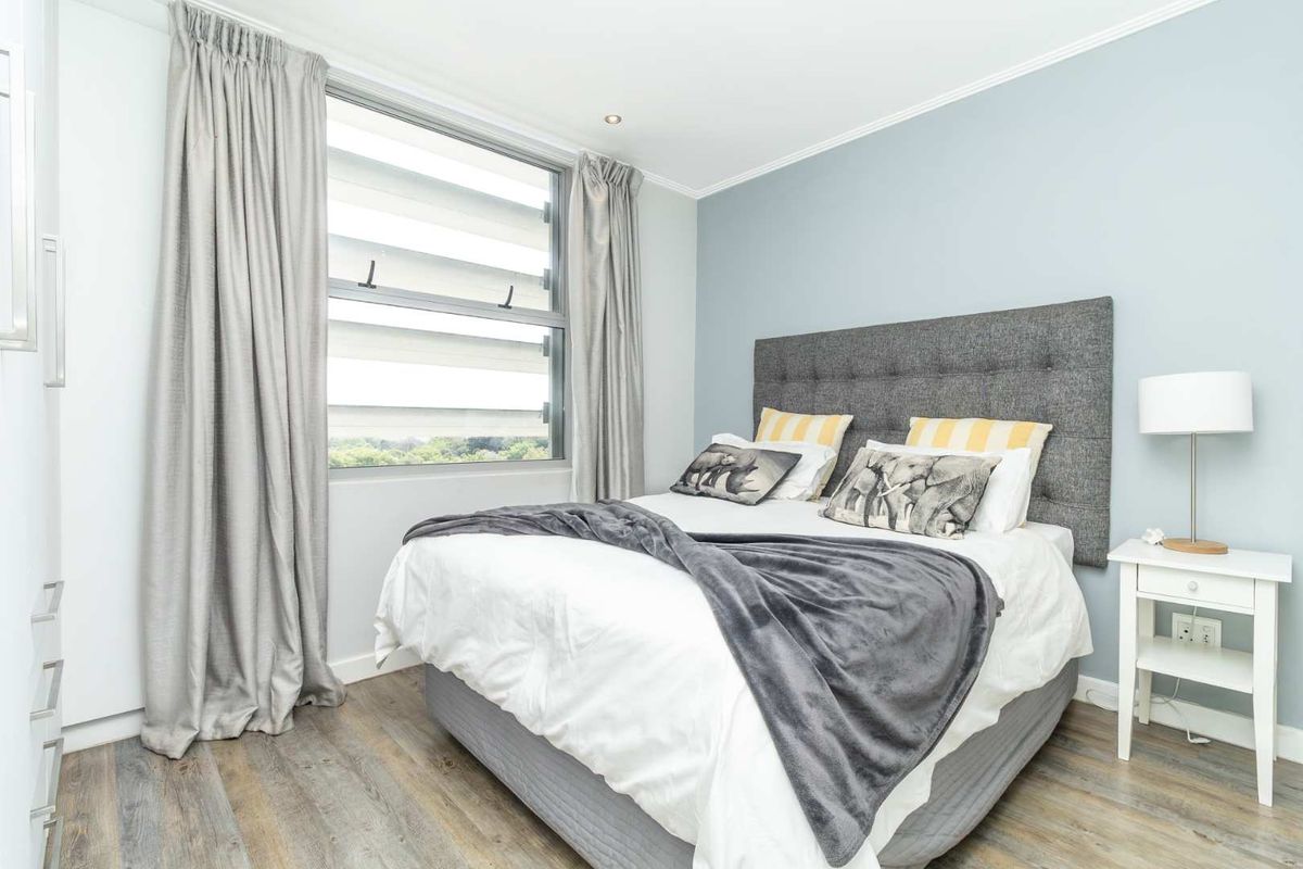 A well-maintained bedroom featuring modern wood-look flooring, a large window with integrated blinds, and a neutral color palette.