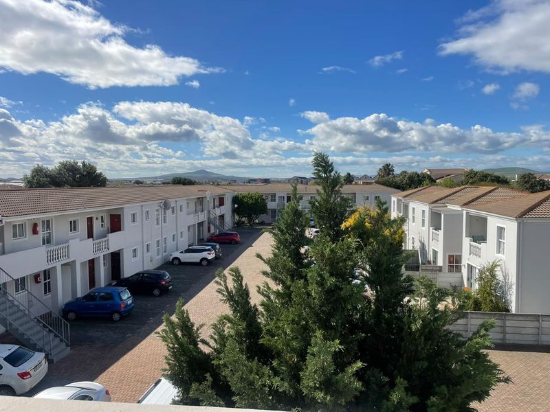 An elevated view of the apartment complex courtyard, featuring paved parking areas, multi-story residential blocks with tiled roofs, and landscaped surroundings.