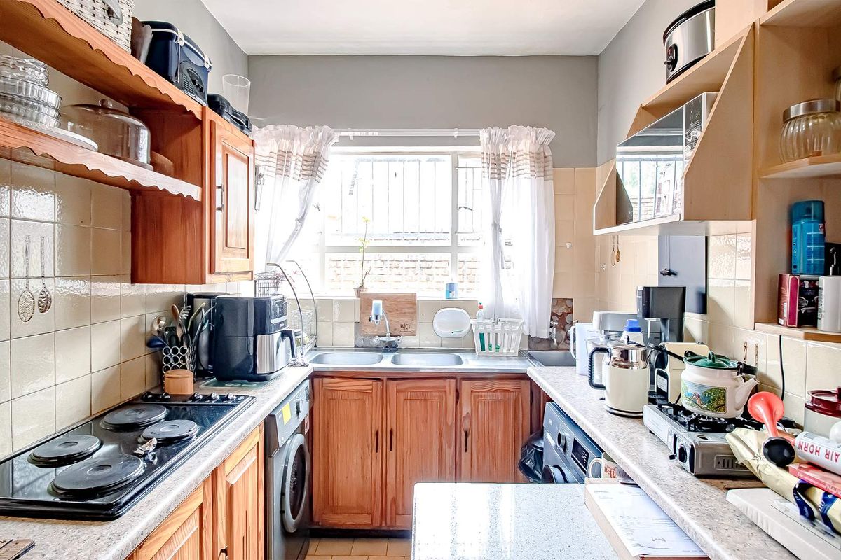 A compact kitchen featuring wooden cabinetry, tiled splashbacks, a double sink, and integrated stove hob, offering a functional layout for daily meal preparation.