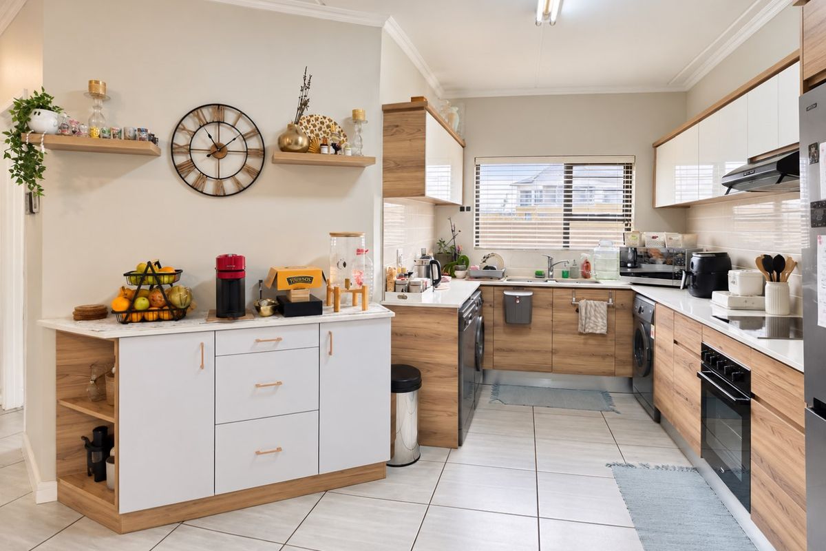 Modern kitchen featuring wood-grain and white cabinetry, tiled flooring, built-in oven, extractor fan, and ample counter space with floating shelving.