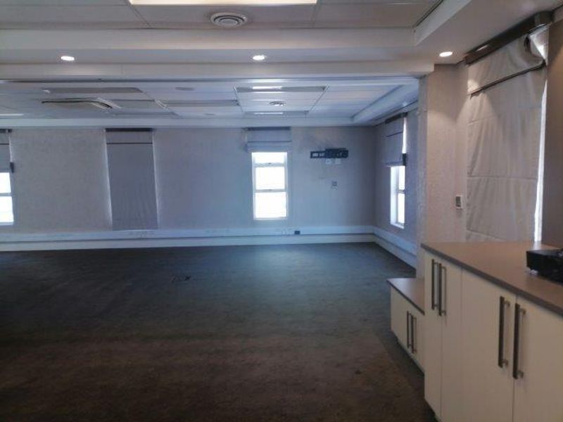 Spacious open-plan office area featuring neutral carpeting, built-in storage cabinetry, recessed ceiling lighting, and large windows with fitted blinds.