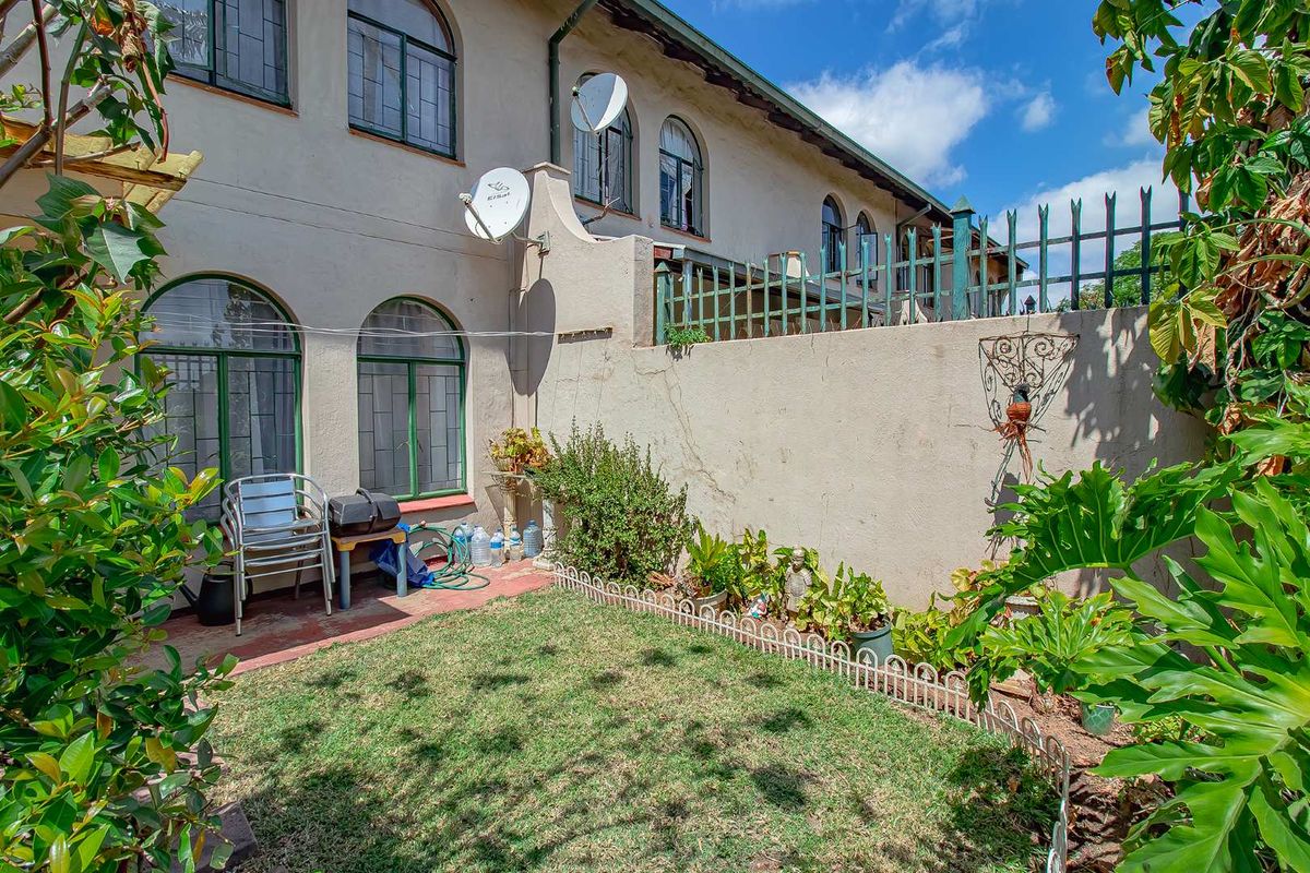 A private rear garden area featuring a small lawn, perimeter wall with metal fencing, and arched windows leading into the townhouse.
