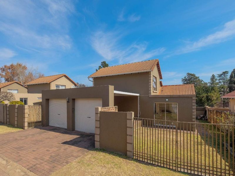 Front view of a two-story residential property featuring a double garage, paved driveway, and secure perimeter fencing.
