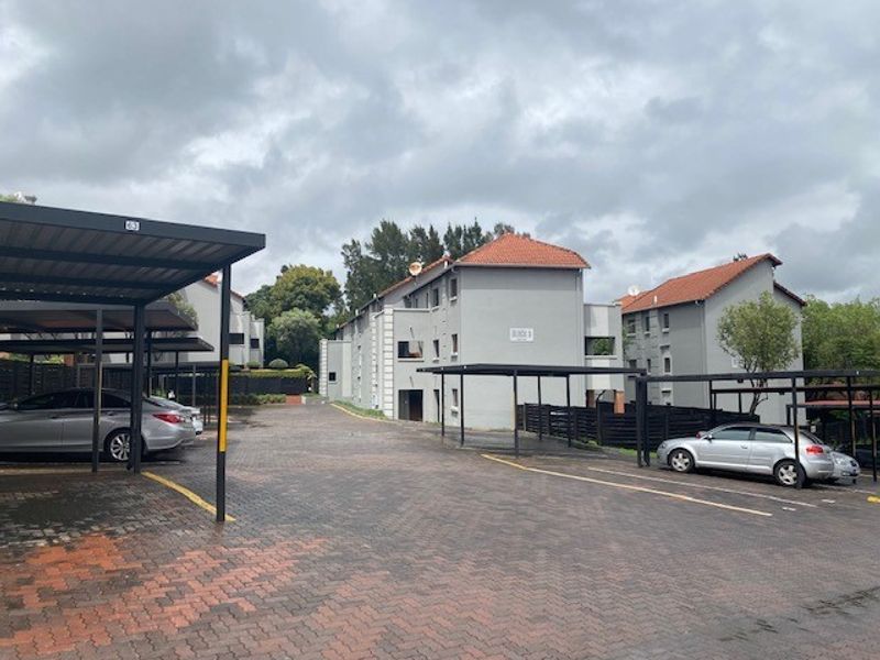 Exterior view of an apartment complex featuring a paved driveway and multiple covered parking bays.