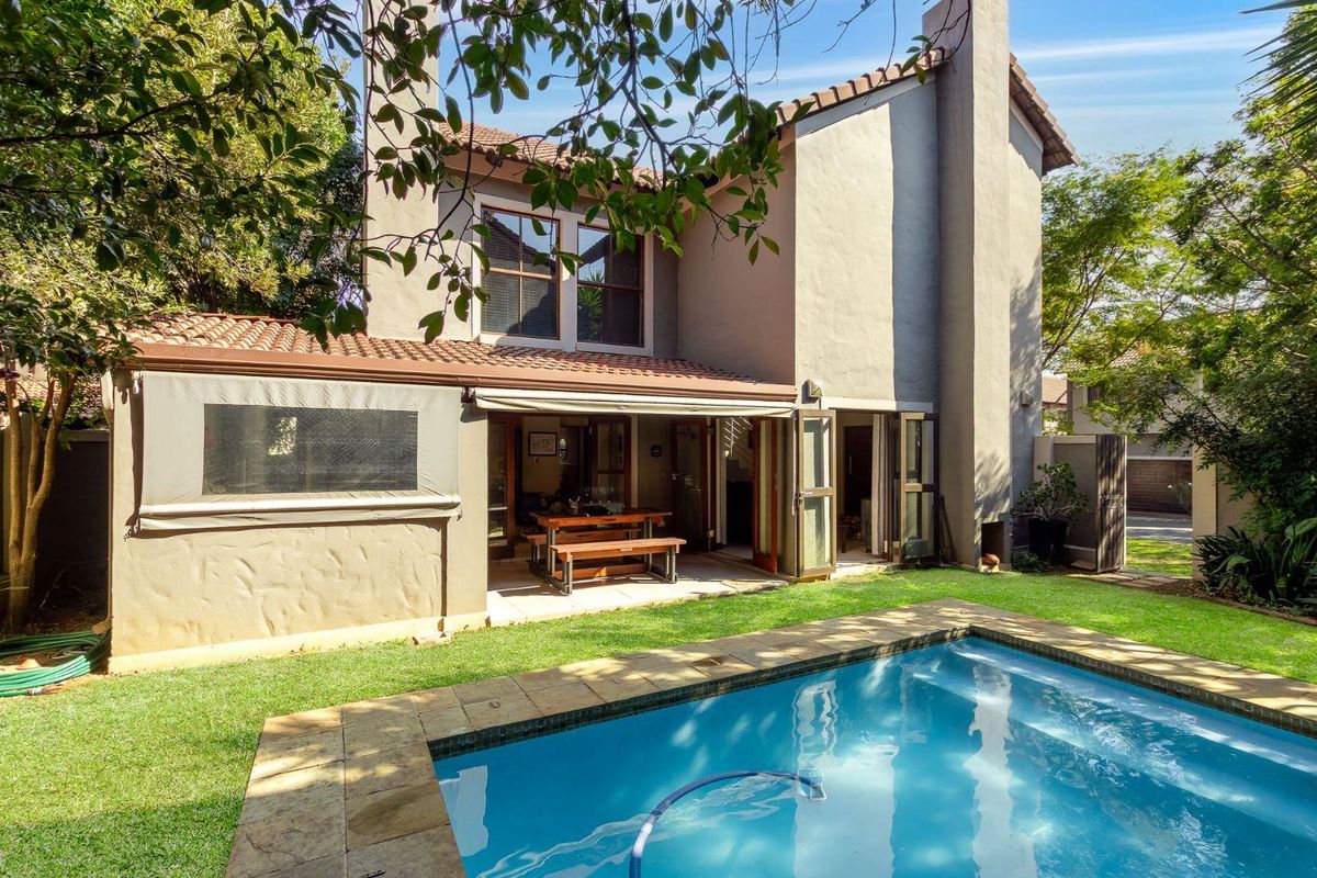 Rear view of the property featuring a swimming pool with stone coping, a covered patio area, and a multi-story structure with a tiled roof.