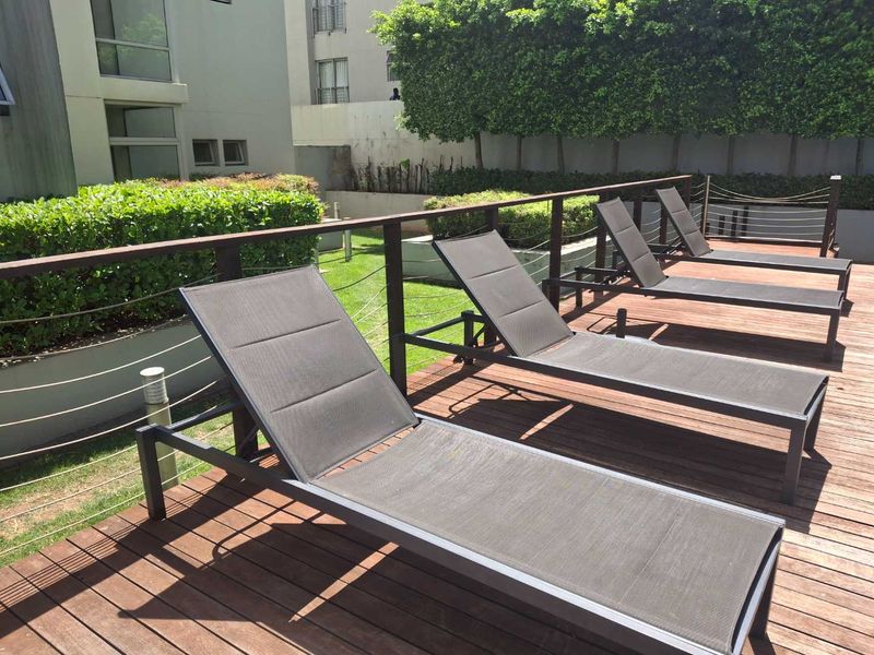 A well-maintained outdoor pool deck featuring timber flooring and modern wire balustrading, set against a landscaped garden backdrop.