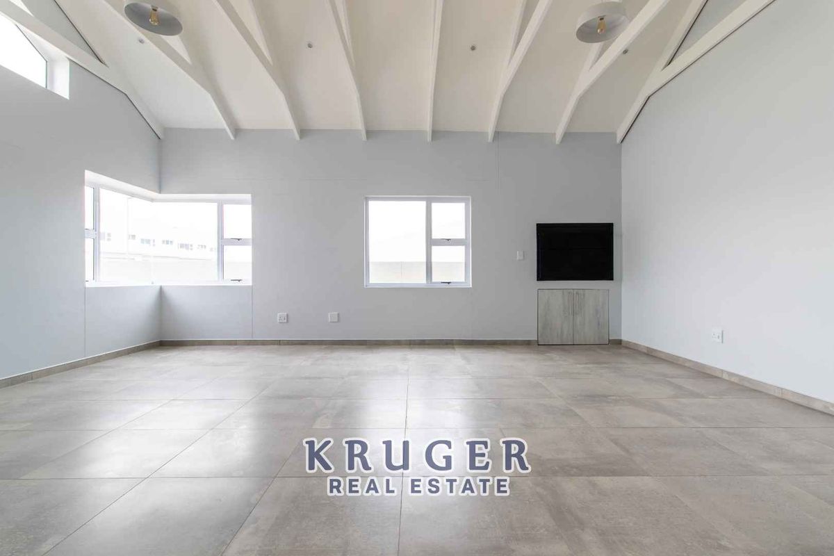 Spacious living area featuring high vaulted ceilings with exposed beams, large windows for natural light, and modern tiled flooring.