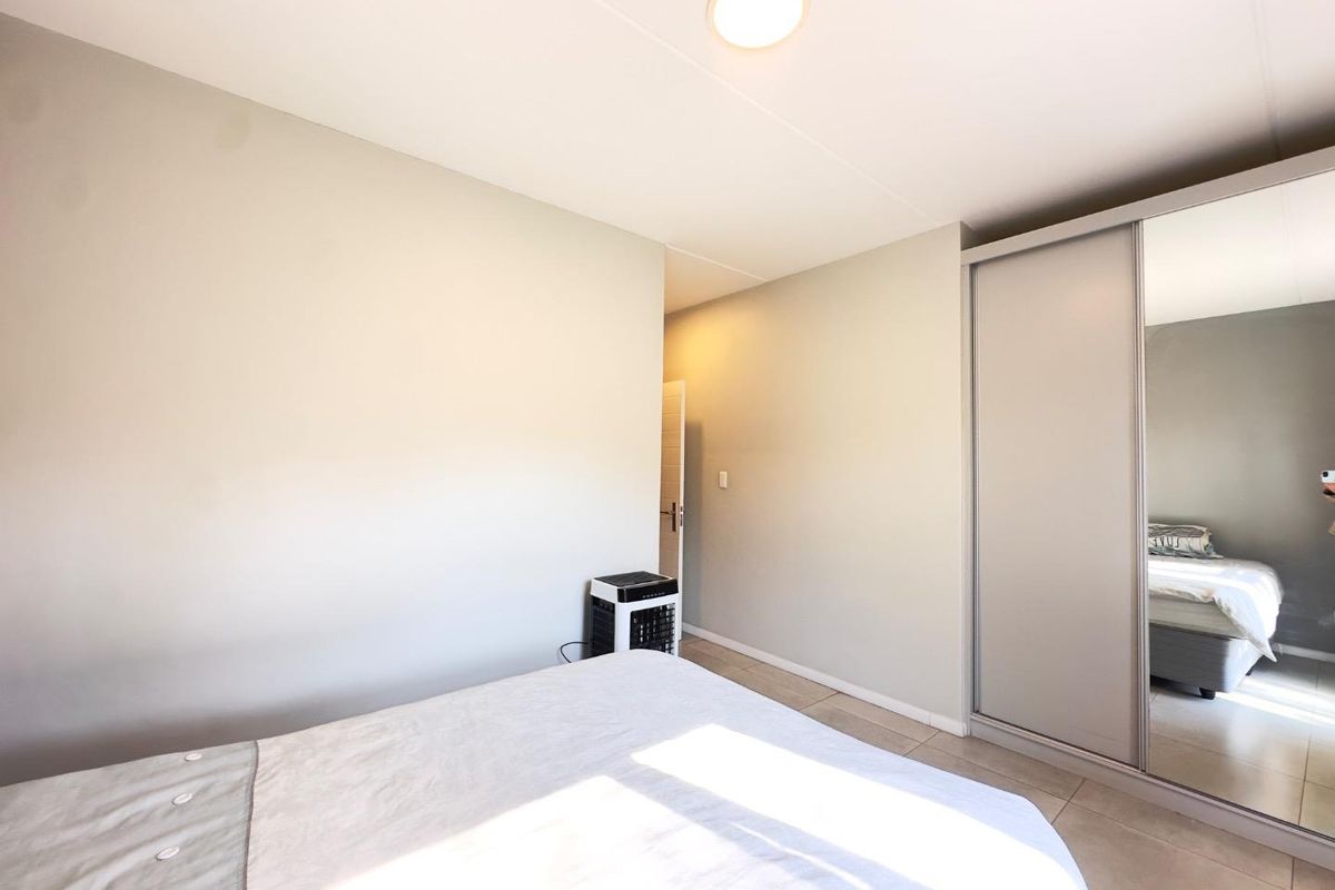 A clean, neutral bedroom featuring tiled flooring and a large built-in sliding door wardrobe with a mirrored panel.