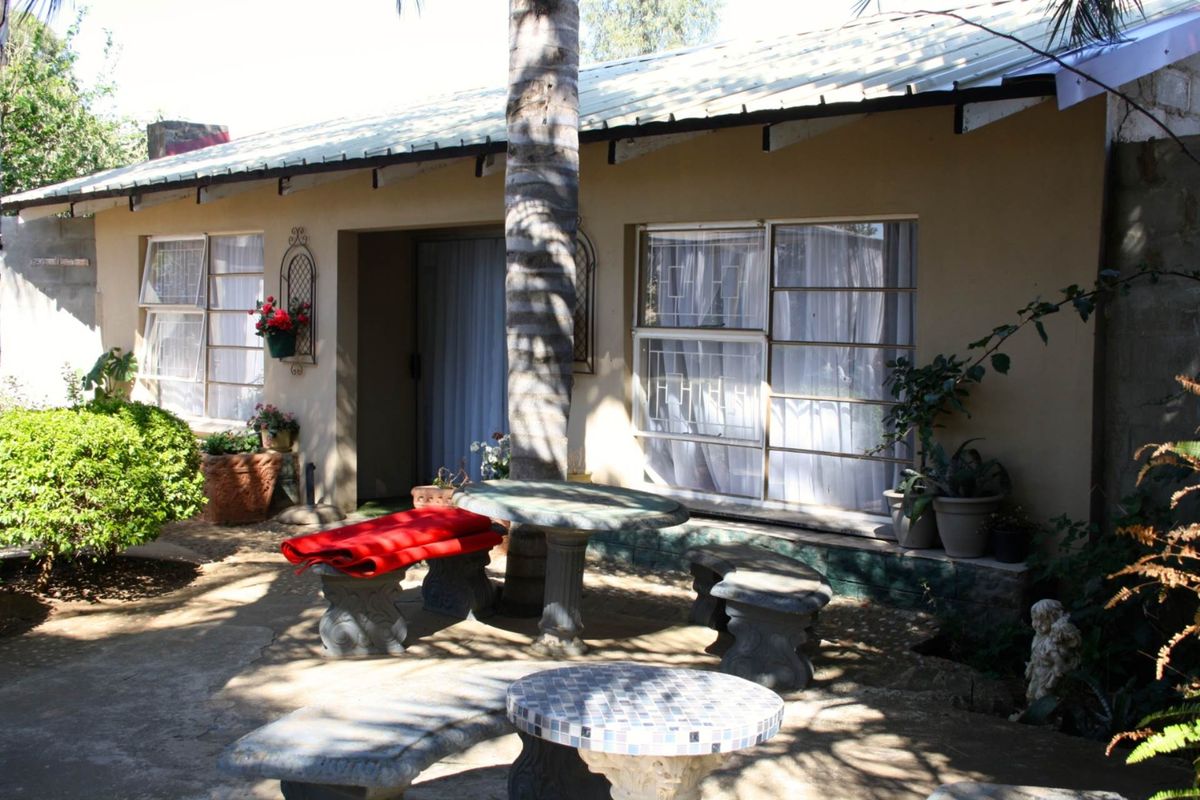 A rear exterior view of a farm-style dwelling featuring a paved patio area, metal roof, and large windows with security bars.