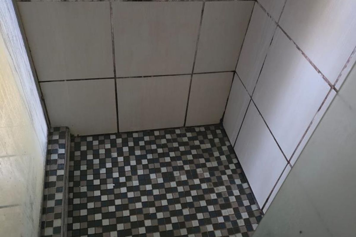 A shower enclosure featuring mosaic floor tiling and white wall tiles, showing signs of wear and discolored grout.