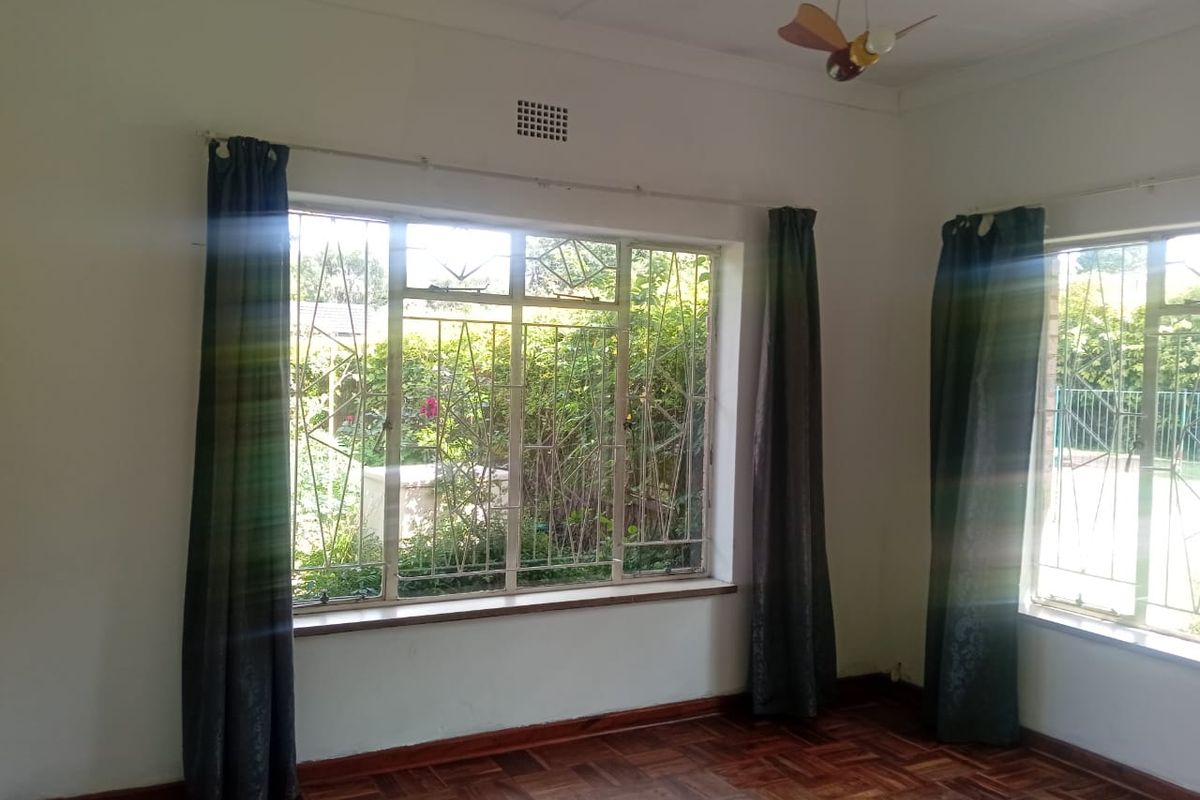 Bright living area featuring classic parquet flooring, large steel-framed windows with security bars, and neutral wall finishes, offering a blank canvas for interior design.