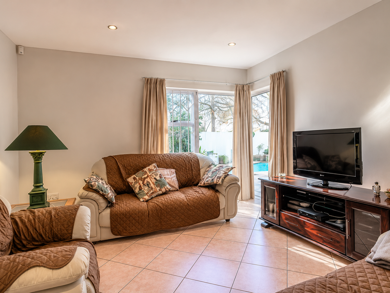 A comfortable living room featuring ceramic tile flooring, recessed lighting, and a sliding glass door providing direct access to the outdoor pool area.
