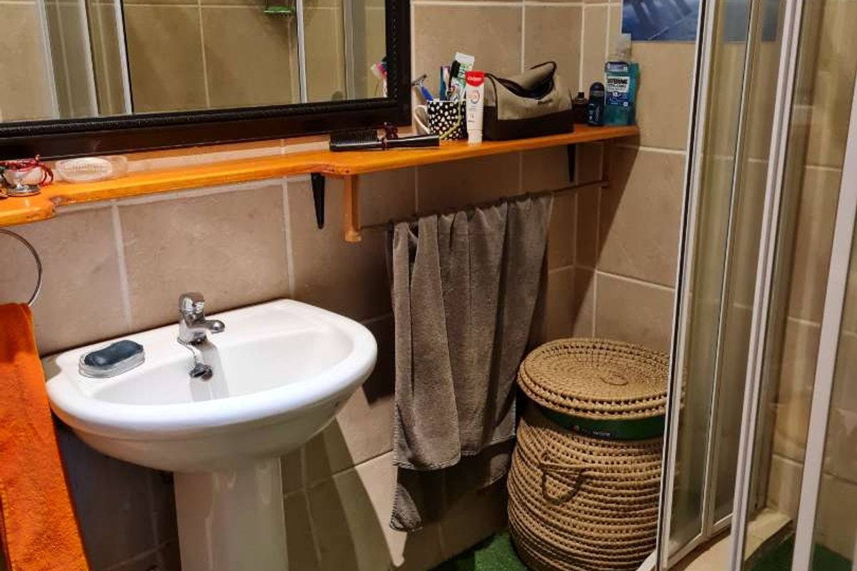 Compact bathroom featuring a pedestal sink, corner shower enclosure, and wall-mounted mirror with integrated shelving.