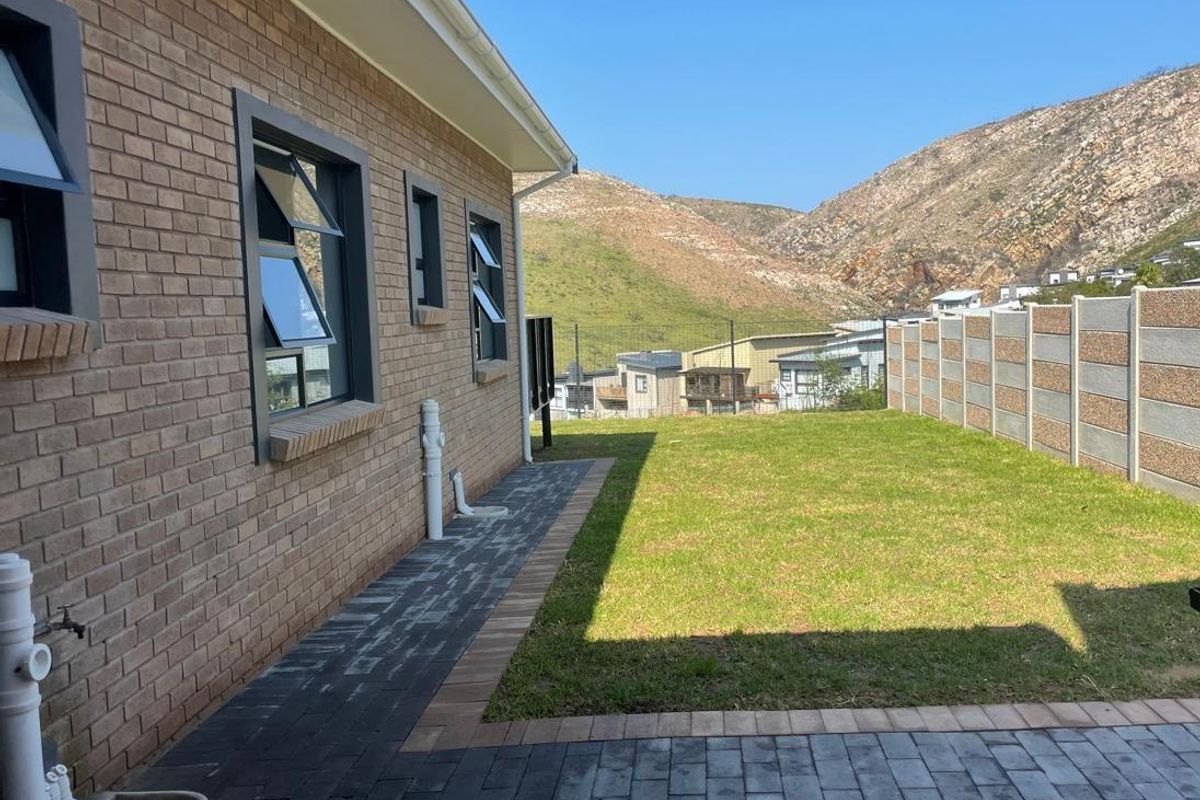 A well-maintained rear exterior featuring a brick facade, paved walkway, lawn, and a precast boundary wall with scenic mountain views.