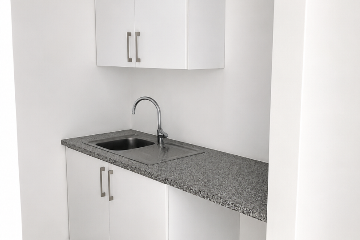 A clean, compact office kitchenette featuring white built-in cabinetry, a granite countertop, and a stainless steel sink.