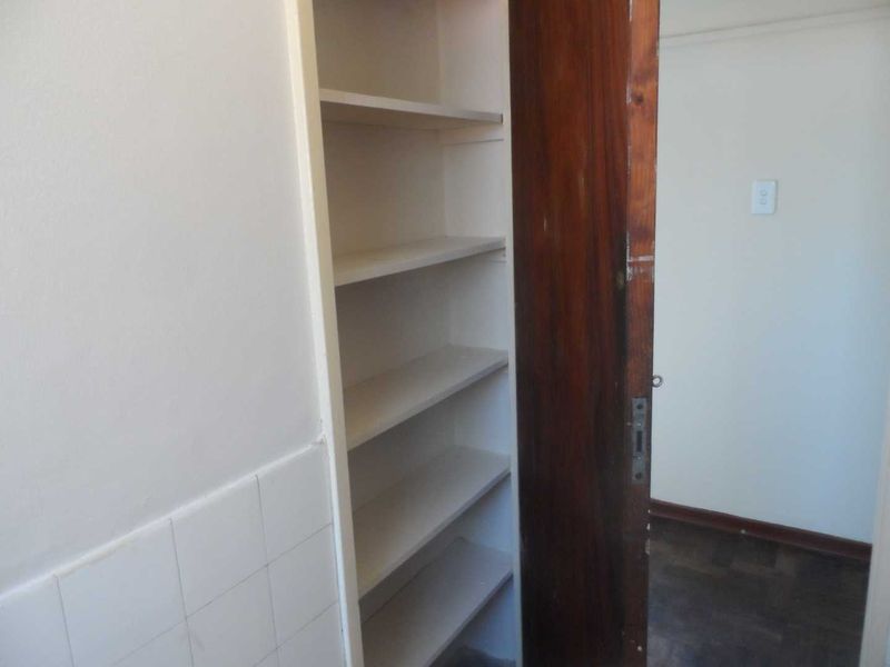 A utility storage cupboard featuring built-in shelving and a wooden door, located adjacent to a tiled wall area.