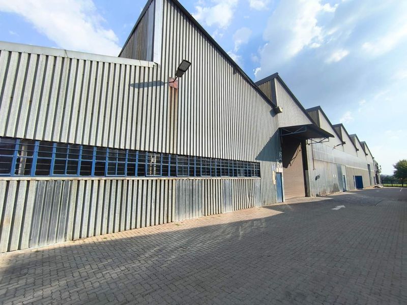 Industrial warehouse exterior featuring corrugated metal cladding, steel-framed windows, and a paved driveway with access via a large roller shutter door.